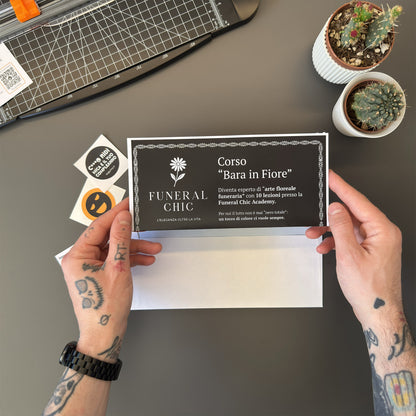 Foto prodotto del finto voucher per il corso per diventare esperti di arte floreale funeraria tenuto tra le mani